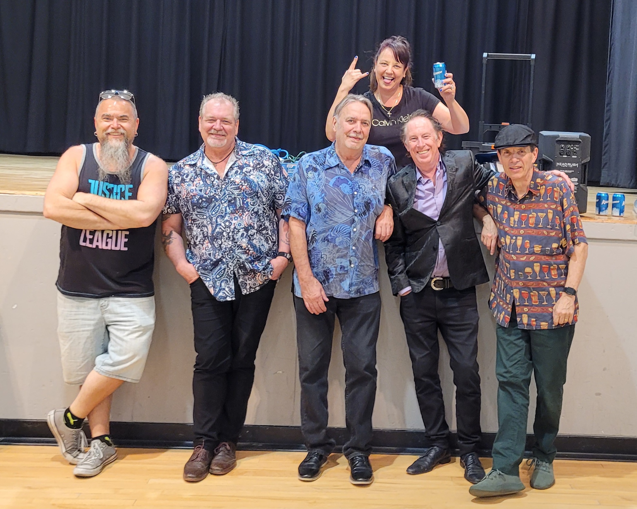 Jack de Keyzer band posing together in front of the stage setup inside a community hall