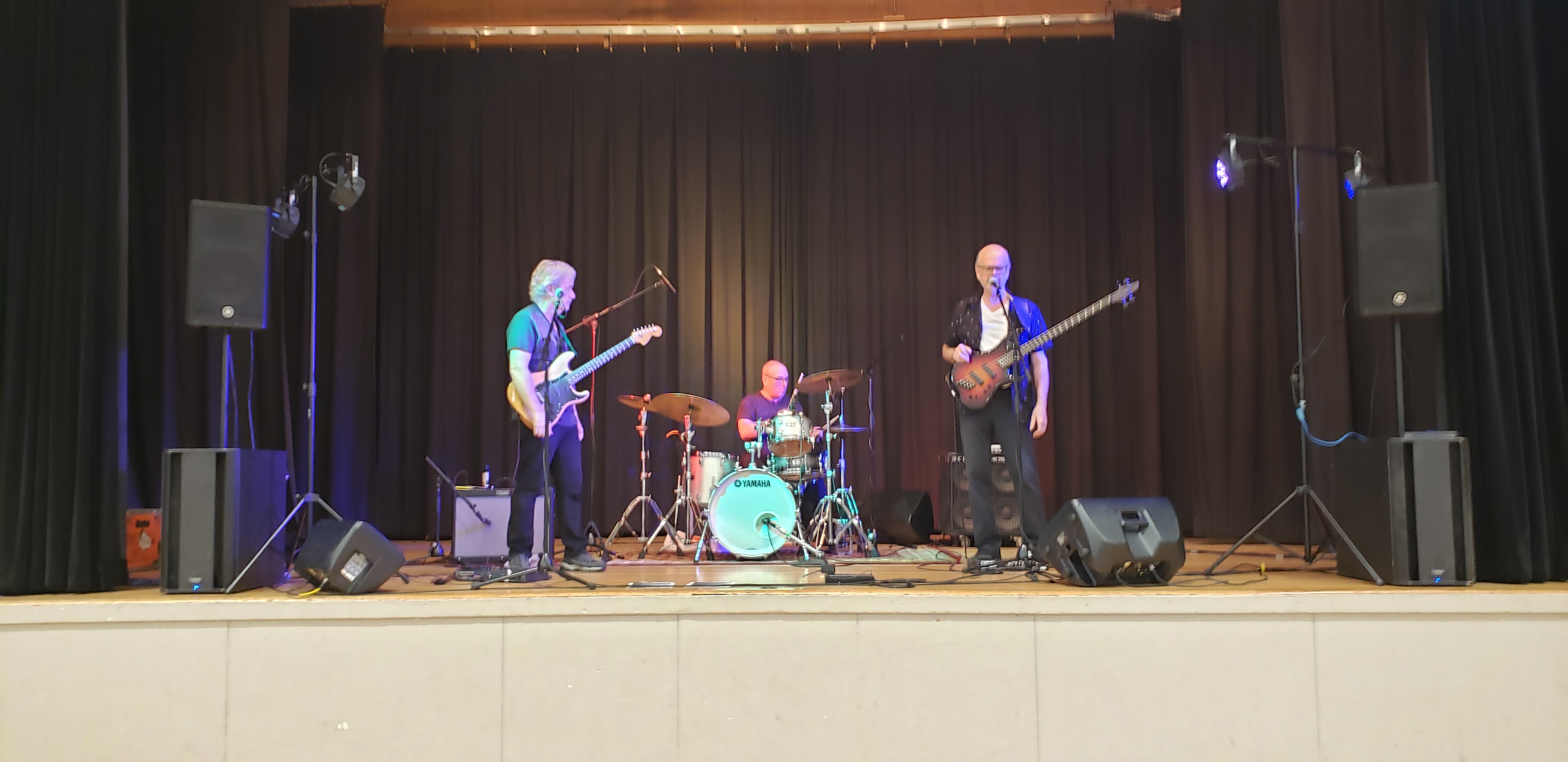 Jack Semple performing live on a theater stage with full audio setup, guitar, drums, and bass